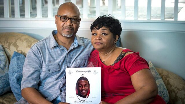 Alvino and Beverly Crawford sit side-by-side holding a celebration of life program for their son, Alvino